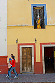 'Young couple walking beneath a skeleton statue on an old Mexican street; Guanajuato, Mexico'