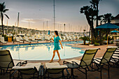 A young girl strolls by the swimming pool with her drink.