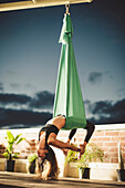 A lady performs aerial yoga.