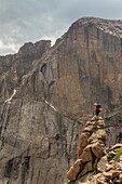 A male hiker standing on a rocky spire below Long's Peak and The Diamond Face in Rocky Mountain National Park, Estes Park, Colorado.