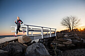 A runner crosses a seaside bridge at sunset.