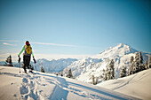 A female snowshoer walks a snow covered ridgeline with Mount Baker in the background.