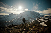 A hiker stands on Burroughs Mountain while the Moon rises over Mount Ranier.