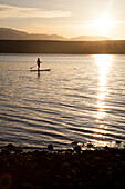 A fit male paddles his stand up paddle board (SUP) along the Hood Canal in the Puget Sound near Poulsbo, Washington at sunset.