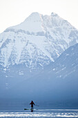 A man stand up paddle boards (SUP) on a calm Lake McDonald at sunrise in Glacier National Park near West Glacier, Montana.