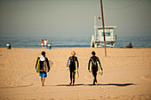Three young boys on  Santa Monica beach are going to do some surf.