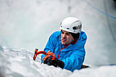 Man with blue jacket and orange ice axes lead climbing an ice fall in Simplon Pass shooted from above. Valais, Switzerland.