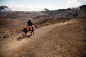 Two men on horseback ride into Haleakala crater.