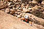 A female climber searches for handholds while finishing the traverse on Sidewinder (5.10b) in Joshua Tree National Park, California.
