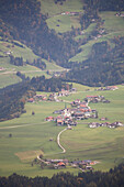 'An alpine village in a valley with green meadows, rolling hills with trees in autumn; Brandenburg, Austria'