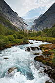 'Water rushing in a river in a valley of trees between the mountains; Olden, Norway'