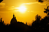 'Glowing sun in a golden sky with silhouettes of dome rooftops; Barcelona, Spain'