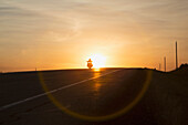 'Man riding a motorcycle at sunset on Alberta highway near Edmonton; Alberta, Canada'