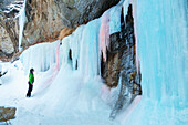 'A woman hiker looks up at a frozen ice fall of pink and blue ice in Plateau Canyon; Palisade, Colorado, United States of America'