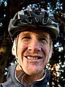'Cyclist wearing helmet with splashes of mud on his face; England'