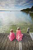 Zwei Mädchen sitzen eingewickelt in Handtüchern auf einem Steg am Starnberger See, Oberbayern, Bayern, Deutschland