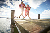Two girls running along a jetty at lake Starnberg, Upper Bavaria, Bavaria, Germany