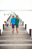 Two boys arm in arm walking along a jetty, lake Starnberg, Upper Bavaria, Bavaria, Germany