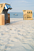 Roofed wicker beach chairs at Baltic Sea beach, man sitting in boat in background, Schönberger Strand, Probstei, Schleswig-Holstein, Germany