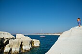 woman and sailboat at the white sandstone cliffs of Sarakiniko beach at Milos in Greece