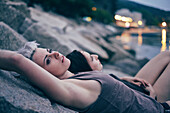 Two young women lying on harbor rocks at dusk