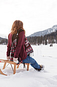 Young woman sitting on a sled, Spitzingsee, Upper Bavaria, Germany