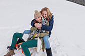 Two young women sitting on a sled, Spitzingsee, Upper Bavaria, Germany