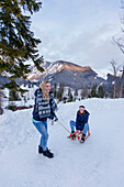 Young woman pulling a sled with woman, Spitzingsee, Upper Bavaria, Germany