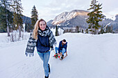 Young woman pulling a sled with woman, Spitzingsee, Upper Bavaria, Germany