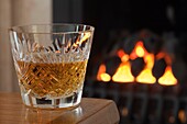 Dram of whiskey in a cut crystal glass on a table by an open coal fire
