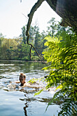 young man swimming in the Wakenitz river, along the former German border between East and West, area so called Amazona of the North, Schleswig-Holstein, Germany