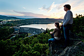 Two people enjoying the view of Edertalsperre dam at Lake Edersee in Kellerwald-Edersee National Park at sunset, Lake Edersee, Hesse, Germany, Europe