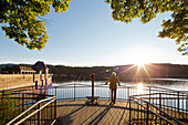 Mann steht auf einer Aussichtsplattform im Licht der tiefstehenden Sonne und blickt zur Sperrmauer Edertalsperre am Edersee im Nationalpark Kellerwald-Edersee, Nordhessen, Hessen, Deutschland, Europa