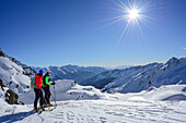 Two persons back-country skiing looking towards Zillertal Alps and Stubai Alps, Schneespitze, valley of Pflersch, Stubai Alps, South Tyrol, Italy