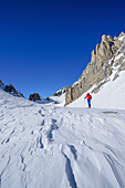 Woman back-country skiing standing beneath rock wall of Monte Sautron, Valle Maira, Cottian Alps, Piedmont, Italy