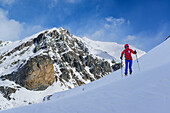 Woman back-country skiing ascending towards Monte Faraut, Rocca Senghi and Monte Ferra in background, Monte Faraut, Valle Varaita, Cottian Alps, Piedmont, Italy
