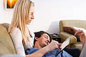 Young couple at home, cuddling on the sofa, playing on the tablet