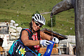 Mountainbikerin füllt Wasservorrat an einem Brunnen auf, Trentino, Italien