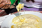 Polenta mit Käse überbacken, Käse zieht Fäden zwischen Teller und Gabel, Trentino, Italien