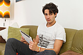 Young man sitting on the sofa, playing on the ipad