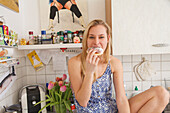 Young woman eating a doughnut in the kitchen