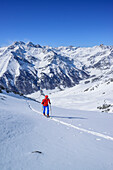 Woman back-country skiing ascending towards Punta Tre Chiosis, view to Val Varaita with Chianale, in background Monte Salza, Cima di Pienasea and Tete des Toilliers, Punta Tre Chiosis, Valle Varaita, Cottian Alps, Piedmont, Italy