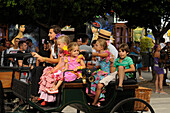 Familie mit Kindern in in Flamenco Kleidern in Pferdekutsche auf der Feria, Malaga, Andalusien, Spanien