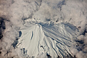 Mount Egmont in winter covered with snow and surrounded by clouds, Taranaki, New Zealand
