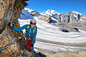 Woman climbing the via ferrata at Piz Trovat with view to Piz Palue (3905 m), Bellavista (3922 m), Piz Bernina (4049 m), Piz Morteratsch (3751 m) as well as Pers- and Morteratsch glacier, Engadin, Grisons, Switzerland
