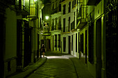 Lonesome woman walking by night in a dimly lit alley with green light in Priego de Cordoba, Sierra Subeticas, Córdoba province, Andalusia, Spain