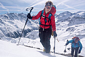 Zwei junge Bergsteigerinnen mit Steigeisen, Stock und Pickel steigen die verschneite Südwestflanke des Mont de l‘Etoile hoch, rechts im Hintergrund der Gipfel der Pigne d‘Arolla, Val d‘Hérens, Walliser Alpen, Kanton Wallis, Schweiz