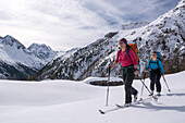 Zwei junge Skitourengängerinnen ziehen ihre Aufstiegsspur in den frischen Tiefschnee, im Hintergrund der Gipfel des Mont Collon, Val d‘Hérens, Walliser Alpen, Kanton Wallis, Schweiz