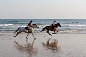 Two young women horse-riding along beach, Algarve, Portugal