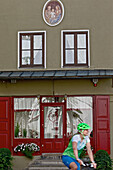 Fahrradfahrerin fährt an einem Haus mit einer roten Tür vorbei, Burghausen, Chiemgau, Bayern, Deutschland
